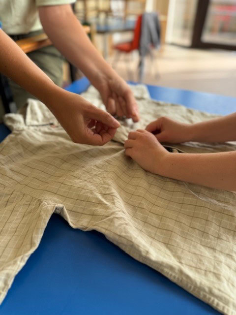 An occupational therapist helping a child to button up a beige shirt. The shirt is lying flat on the table and two pairs of hands are working together to button it up.